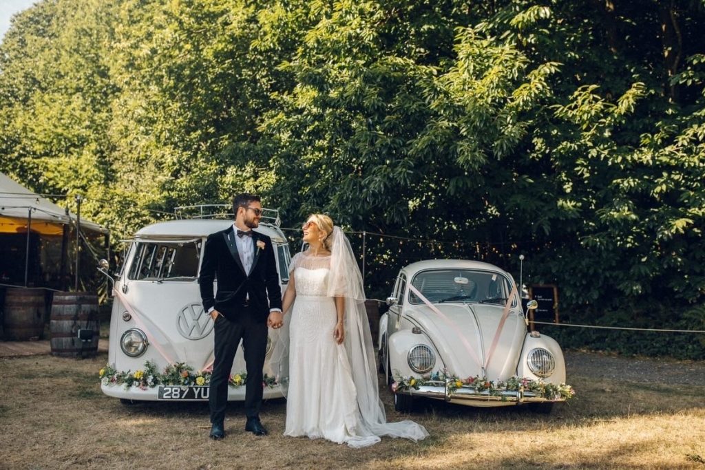 Couple standing infront of VW Beetle and Camper Van