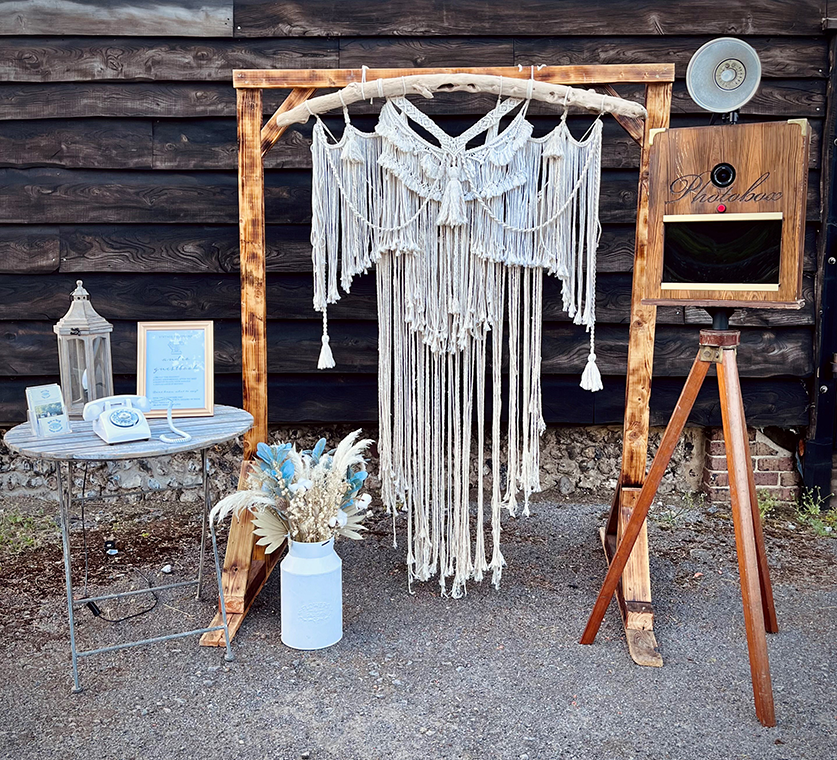 Image shows a wooden stand with macrame hanging and a vintage open air photobooth