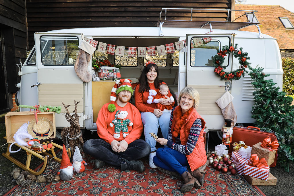One man and two ladies sit in front of a camper van decorated in christmas decorations.