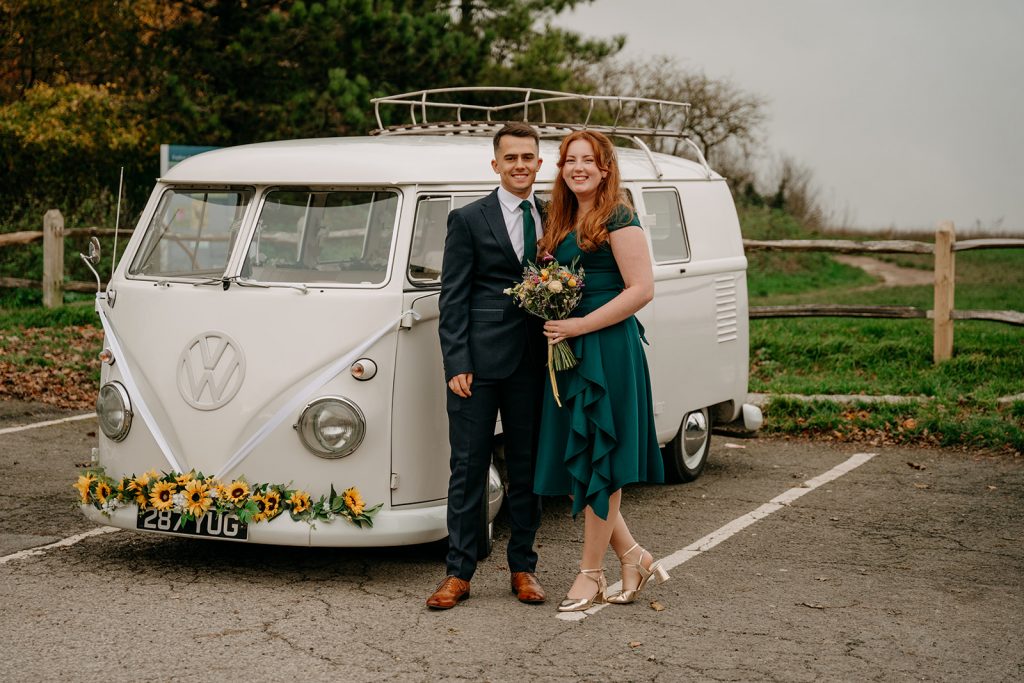 Phoebe Rossi Photography - Camoer van wedding car with happy couple stood infront.